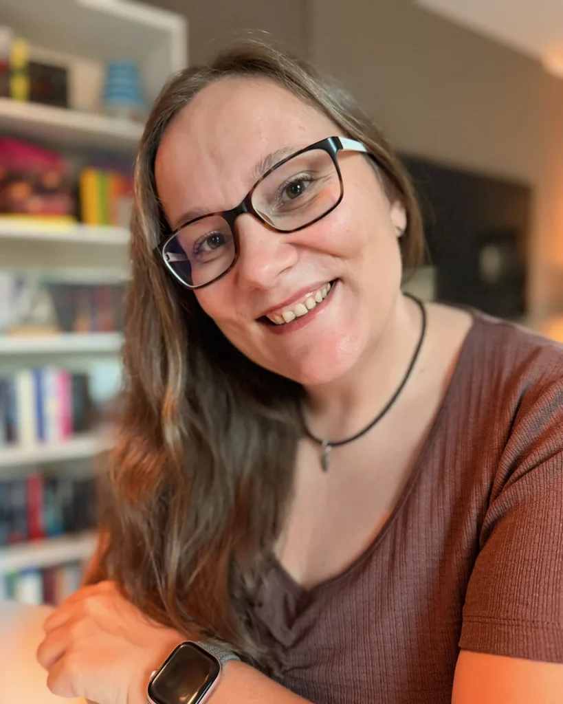 Maria Lengemann lächelnd am Schreibtisch vor ihrem Bücherregal